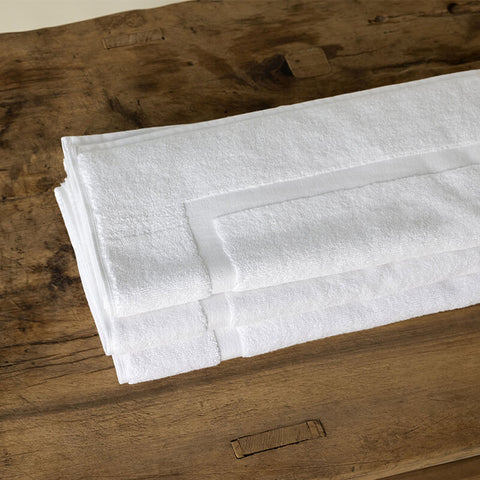 Weiße Badematte aus hochwertigem Baumwollfrottee auf einer Holzoberfläche, geeignet für stilvolle Badezimmer und Hotelbäder.