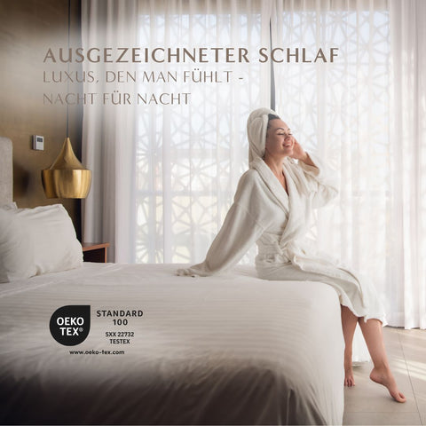 Frau sitzt entspannt auf dem Bett und genießt den Komfort des Excellence Gänsedaunenkopfkissens für erholsame Nächte und luxuriösen Schlaf.