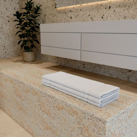 Premium Luxushotel Badematten 3er Set mit sauber gefalteten weißen Badematten auf einer Natursteinbank in einem modernen Badezimmer.