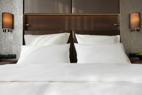 Nahaufnahme der ordentlich arrangierten weißen Kopfkissen auf einem Bett, bezogen mit glattem Premium Bettdeckenbezug vor einem strukturierten, gepolsterten Kopfteil in einem Hotelzimmer.