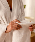 Person im Bademantel hält ein weiches Handtuch aus dem Premium Luxushotel-Handtücher 4er Set für komfortable Körperpflege und Wellnessmomente.