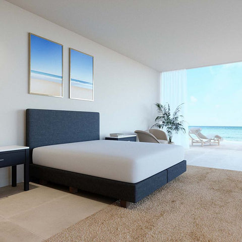 Modernes Schlafzimmer mit weißem Select Spannbettlaken auf einem eleganten Boxspringbett vor heller Fensterfront mit Meerblick