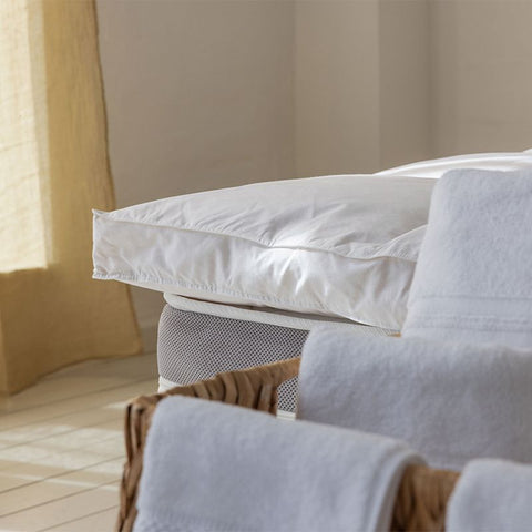 Weiße Bettdecke und Kissen auf einem gemütlich eingerichteten Bett, die ein harmonisches Schlafsystem mit zusätzlichem Topper ergänzen.